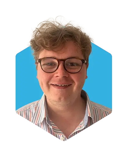 Smiling person with curly light brown hair and glasses, wearing a striped shirt, against a blue background.
